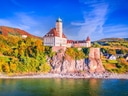 Schloss auf bewaldetem Hügel am Flussufer.