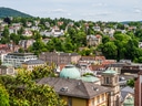 Stadtansicht mit mehreren Häusern und grüner Landschaft im Hintergrund.