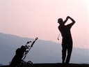 Golfer schlägt Ball, Silhouette bei Sonnenuntergang.