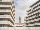 Moderne Gebäude mit verziertem Geländer und Turm im Hintergrund.