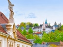 Historische Gebäude mit Statue und Turm, umgeben von Bäumen.