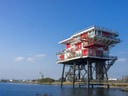 Rotes Gebäude auf Stelzen im Wasser bei blauem Himmel.