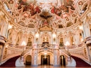 Prunkvoll verzierter Theatersaal mit geschwungener Treppe und Fresken an der Decke.