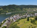 Luftaufnahme eines Dorfes am Fluss mit Hügeln und Weinbergen im Hintergrund.