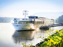 Flusskreuzfahrtschiff auf ruhigem Fluss bei sonnigem Wetter.
