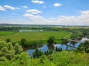 Landschaft mit Fluss, Brücke und grünen Feldern.
