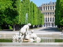 Barocke Gartenstatue und Brunnen vor Schloss mit Bäumen.