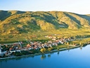 Luftaufnahme eines Dorfes an einem Fluss, umgeben von Hügeln und Weinbergen.