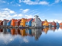 Bunte Häuser spiegeln sich in ruhigem Wasser unter blauem Himmel.