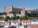 Blick auf eine grosse Burg auf einem Hügel mit roten Dächern und Bäumen.
