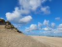 Sanddüne am Strand mit blauem Himmel und Wolken.