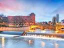 Fluss in Nürnberg mit beleuchtetem Brückenbogen und Gebäuden im Hintergrund.