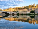 Fluss mit Brücke und historischer Stadtkulisse im Sonnenlicht.