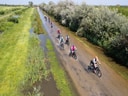 Gruppe von Radfahrern auf nasser Landstrasse neben Kanal und Bäumen.