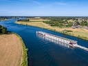 Flusskreuzfahrtschiff auf einem Fluss in ländlicher Landschaft.