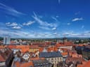 Stadtpanorama mit roten Dächern und blauem Himmel.