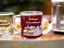 Zwei Tassen mit Weihnachtsmarkt-Motiv, eine mit hellem und eine mit dunklem Getränk.