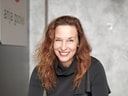 Lächelnde Frau sitzt an Tisch mit Stoffmustern.