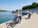 Radfahrer am Flussufer bei blauem Himmel.