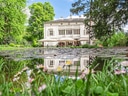 Weisse Villa mit Teich und Blumen im Vordergrund.