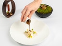 Hand giesst Sauce auf Gourmetgericht neben dekorativen Schalen.
