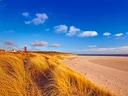 Leuchtturm und Sanddünen an einem sonnigen Strand.