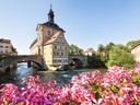 Historisches Gebäude auf einer Brücke über einem Fluss mit rosa Blumen im Vordergrund.