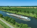 Kreuzfahrtschiff auf einem Fluss mit grüner Landschaft.
