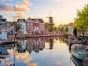 Häuser am Kanalufer mit Windmühle im Hintergrund bei Sonnenuntergang.