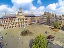 Grosser Platz mit historischem Gebäude und Statue, Menschen spazieren.