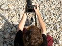 Person sitzt auf Kies und fotografiert.
