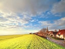 Dorf am Deich bei sonnigem Himmel.