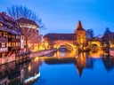 Mittelalterliche Gebäude und Brücke über einem Fluss bei Nacht beleuchtet.