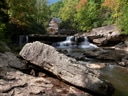 Historische Mühle am Wasserfall in bewaldeter Landschaft.