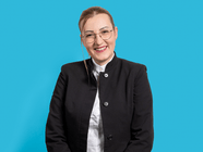 Person in schwarzem Blazer vor blauem Hintergrund.