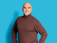 Mann mit braunem Rollkragenpullover vor blauem Hintergrund.
