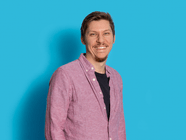 Mann in rosa Hemd vor blauem Hintergrund lächelnd.