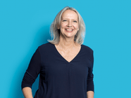 Person mit blonden Haaren vor blauem Hintergrund lächelnd.