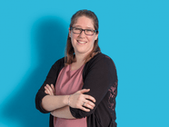Person mit Brille und gefalteten Armen vor blauem Hintergrund.