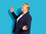 Person in dunkelblauem Blazer vor blauem Hintergrund, lächelt nach oben.