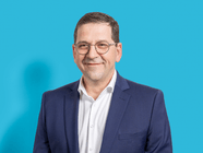 Mann mit Brille in blauem Anzug vor blauem Hintergrund.