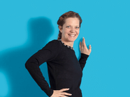 Lächelnde Person in einem schwarzen Kleid vor blauem Hintergrund.
