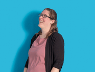 Lachende Person mit Brille vor blauem Hintergrund.