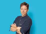 Person in dunklem Hemd vor blauem Hintergrund stehend.