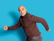 Mann in einem braunen Pullover vor einem blauen Hintergrund, der eine Laufbewegung macht.