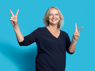 Frau in schwarzem Oberteil zeigt das Peace-Zeichen vor blauem Hintergrund.