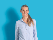 Lächelnde Person mit hellblauer Bluse vor blauem Hintergrund.