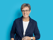 Person mit Brille in einem dunklen Blazer vor blauem Hintergrund.