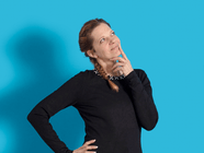 Person in schwarzem Oberteil vor blauem Hintergrund, die nachdenklich schaut.