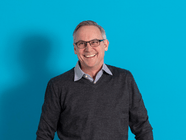 Lächelnder Mann mit Brille vor blauem Hintergrund.